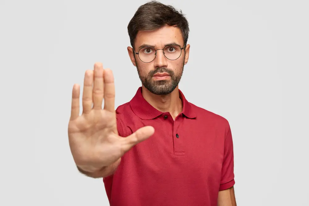 concerned serious bearded man round eyewear pulls palm towards camera stops warns you